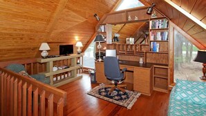 Une chambre confortable située sous les toits, avec un plafond en pente en bois, un bureau avec une chaise, une bibliothèque et un téléviseur.