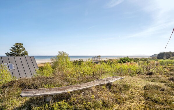 A coastal landscape with a beach, a small building, and a wooden bench. - Cozy home in Glesborg with kitchen (Glesborg)