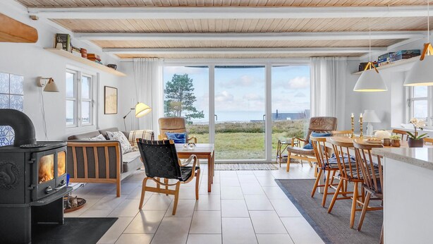 Ett mysigt vardagsrum med en öppen spis, en matplats med trästolar och stora fönster som ger utsikt över omgivningen.