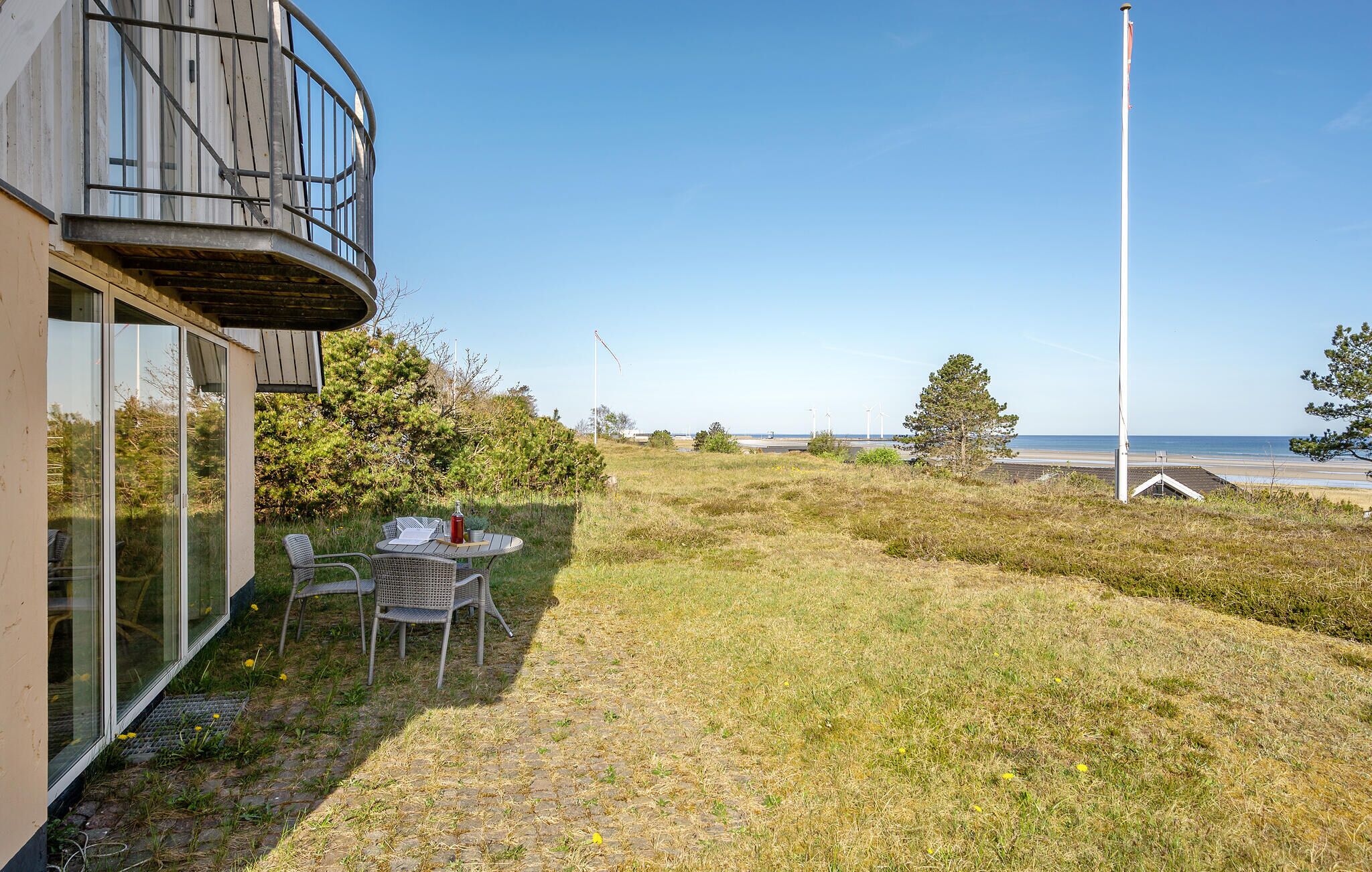 A coastal property with a glass-enclosed balcony, a round outdoor table with chairs, and a view of the beach and ocean.