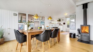 Et moderne køkken med en central ø, hængende lamper og en sort brændeovn.