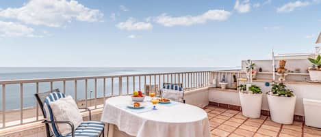 Enjoy a serene sea view from this outdoor space, featuring a round table, striped chair, and cushioned bench.