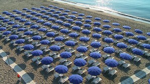 A beach with rows of blue umbrellas and beach chairs.