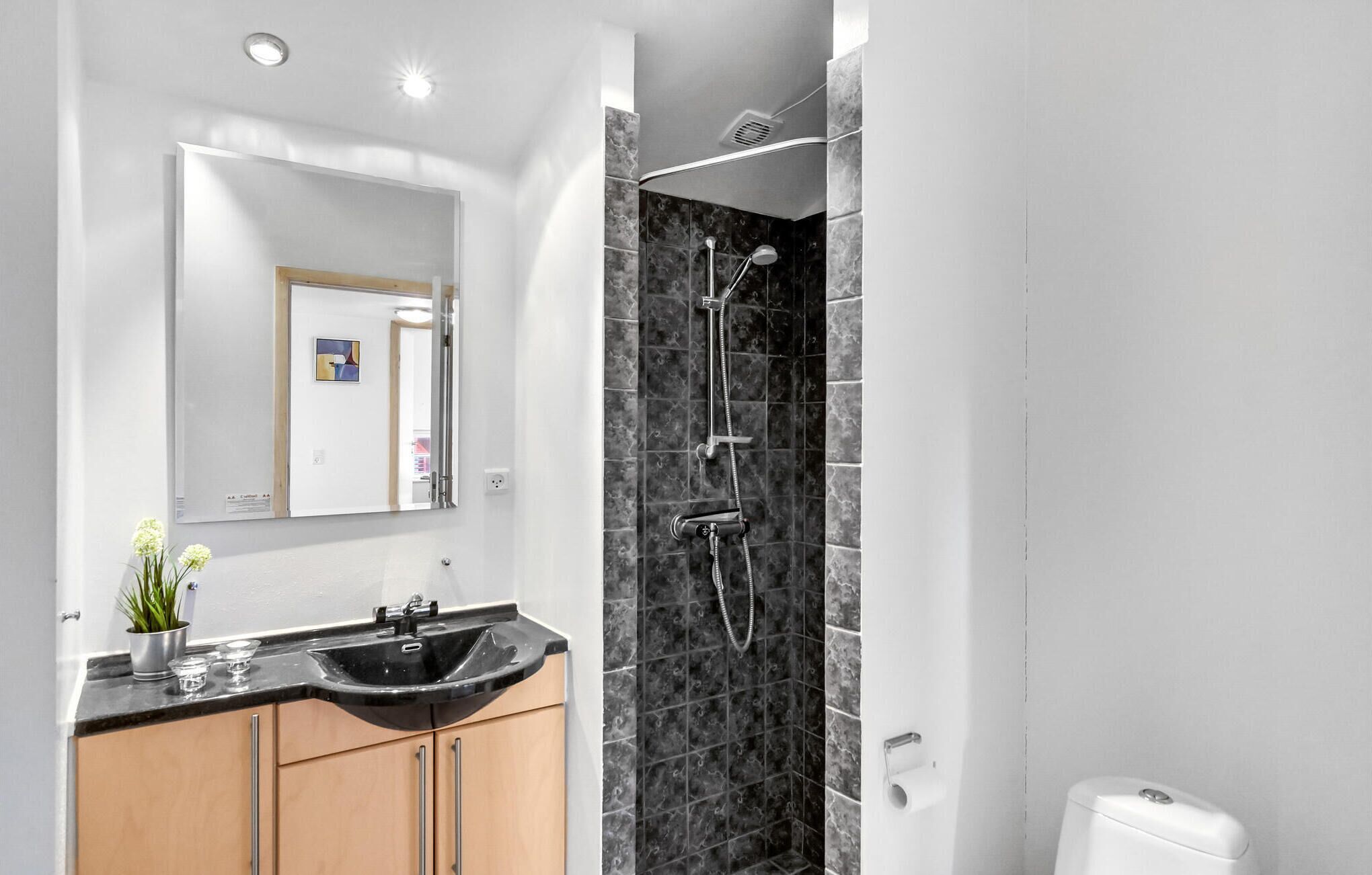 A modern bathroom with a black sink, wooden cabinets, a large mirror, and a shower with a curved design.