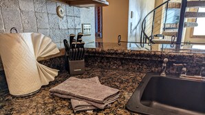 A kitchen with granite countertops, a sink, a knife block, and a towel dispenser.