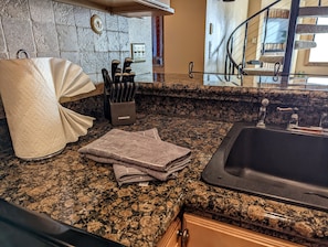 A kitchen with granite countertops, a sink, a knife block, and a towel dispenser.