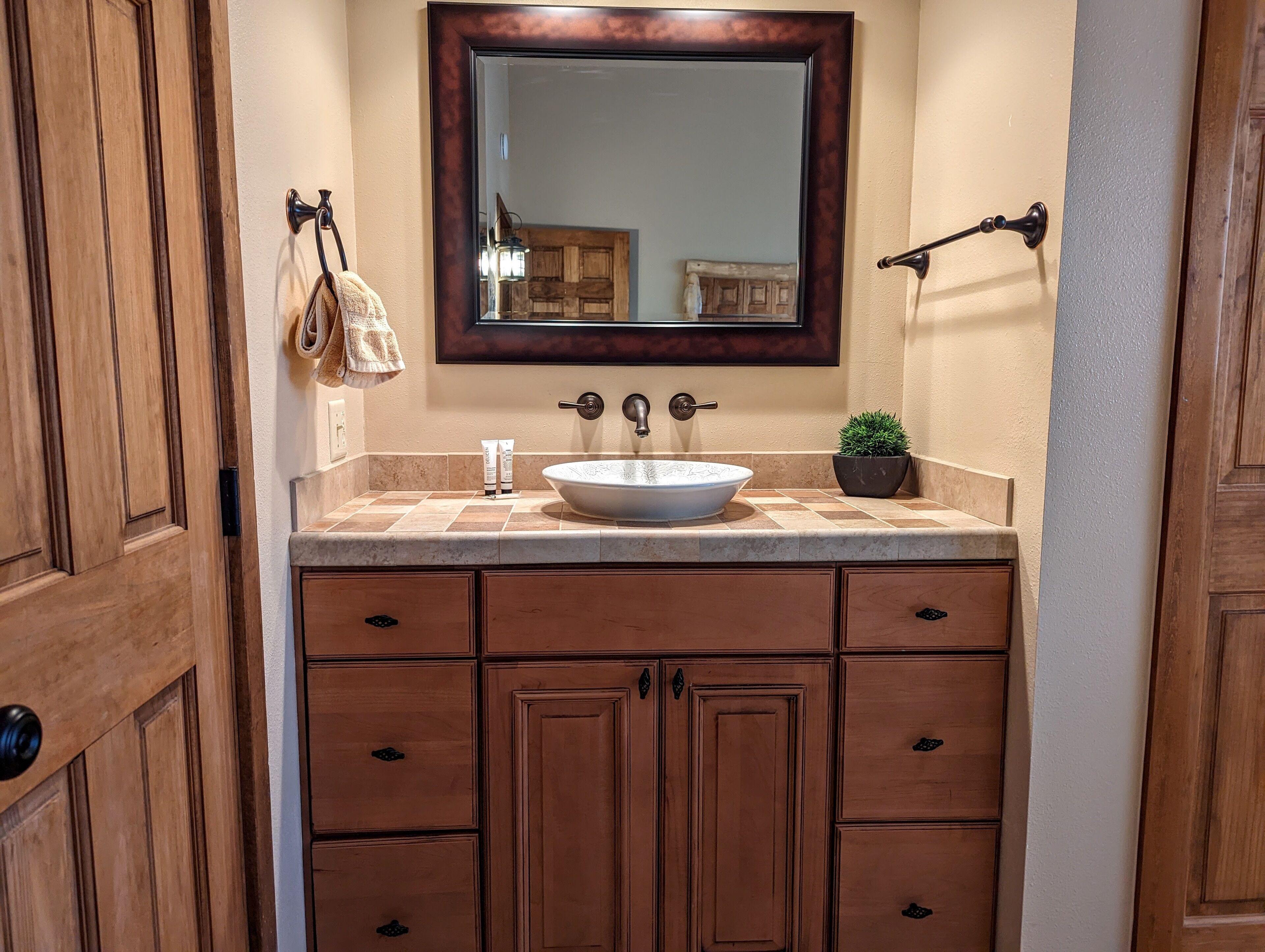 A bathroom with a wooden vanity, a large mirror, a sink, and a potted plant.