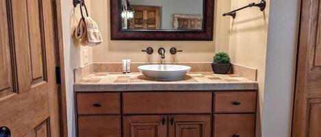 A bathroom with a wooden vanity, a large mirror, a sink, and a potted plant.