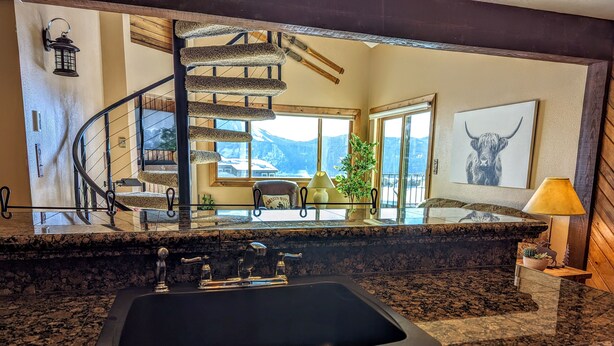 A kitchen with granite countertops, a black sink, and a view of a mountain landscape through large windows.