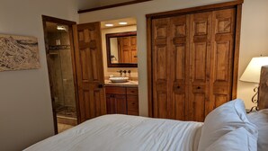 A bedroom with a large bed, wooden wardrobe, and a bathroom with a sink and mirror.