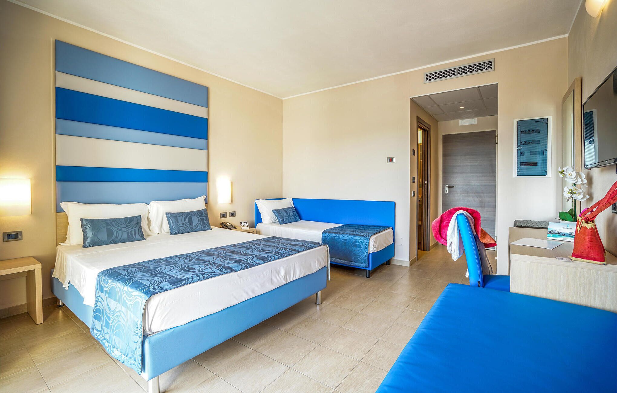 Habitación de hotel con dos camas, un escritorio y un baño visible a través de una puerta abierta.