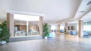 A spacious lobby with a glass partition, seating areas, and potted plants.