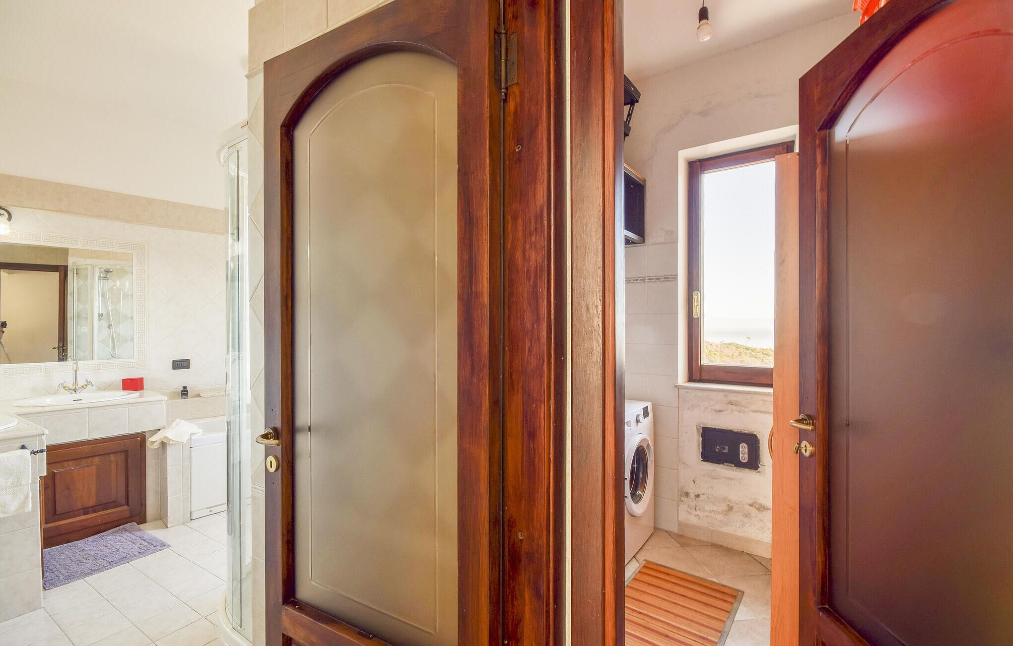 Un baño con puerta de madera, ducha, lavabo y ventana con vistas.