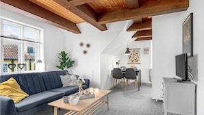 Un soggiorno moderno con un divano blu scuro, un tavolino in legno e un'area pranzo con un armadietto bianco e una televisione.