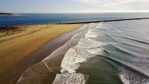 Een strand met golven die de kust naderen, een heldere lucht en een verre kustlijn.