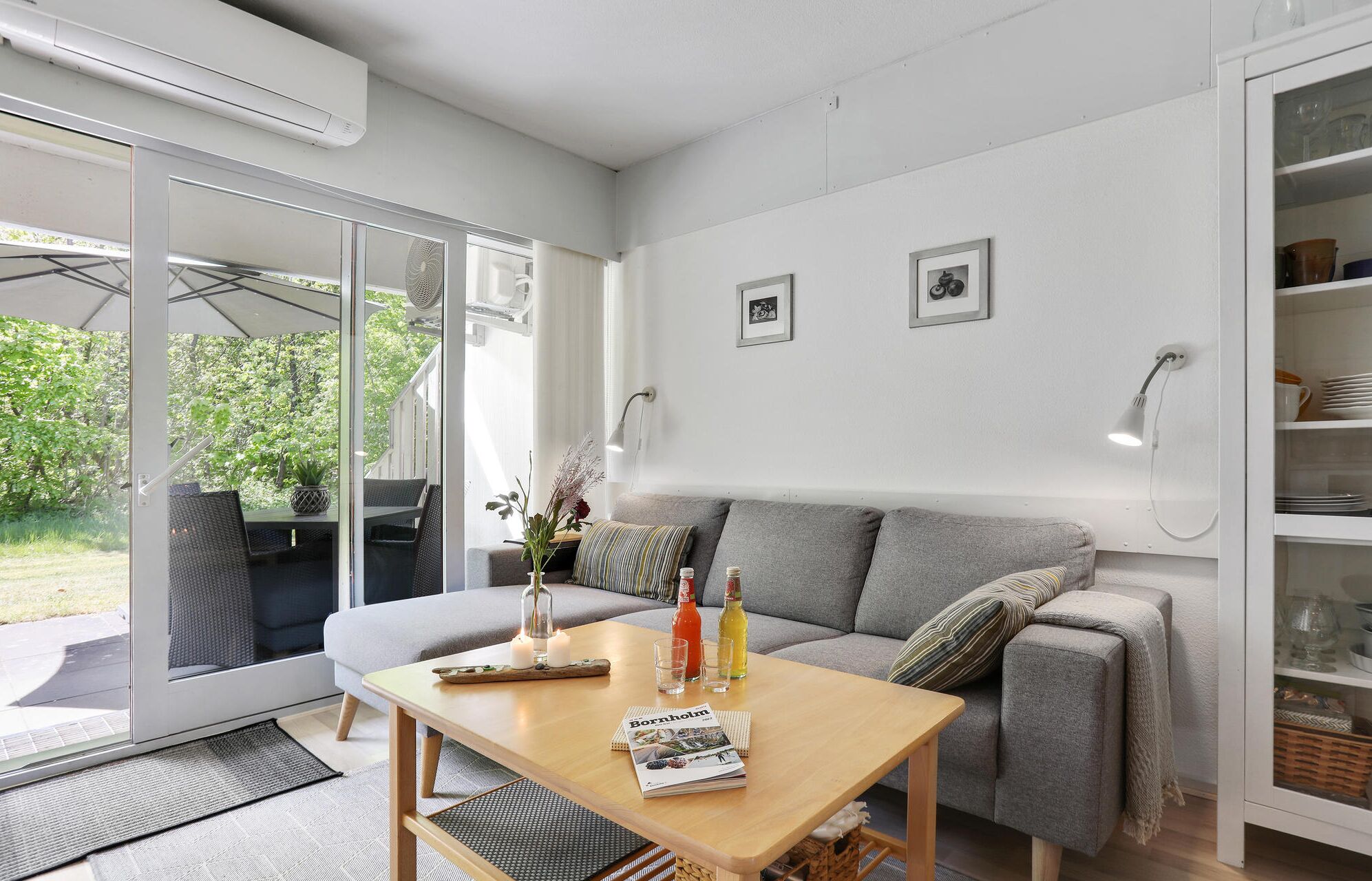 A modern living room with a grey sofa, a wooden coffee table, and a glass door leading to an outdoor patio.