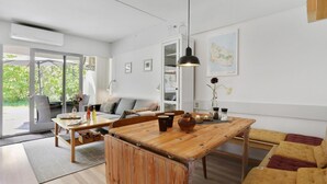 A modern living room with a wooden dining table, a sofa, and a large window overlooking greenery. - Stunning apartment in Hasle (Hasle)