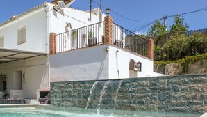 A pool with a waterfall feature, a white building with a balcony, and a stone wall. - Pet friendly home in Sayalonga (Sayalonga)