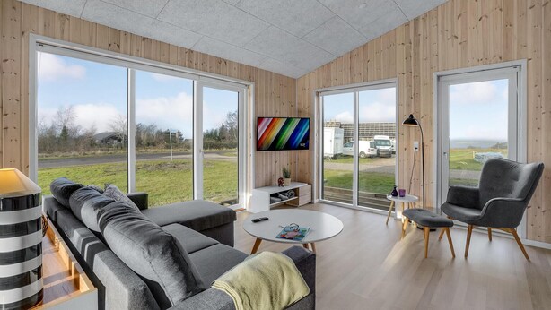 A modern living room with a large TV, comfortable seating, and large windows offering a view of the outside.