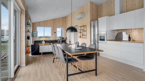 A modern kitchen with wooden paneling, a dining area with a black table and chairs, and a large window providing a view of the outdoors.