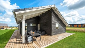 A modern house with a covered patio, a dining area with a table and chairs, and a view of the surrounding landscape.