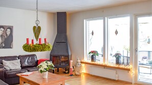 Een gezellige woonkamer met een open haard, een bank, een bijzettafeltje en een raam met planten.