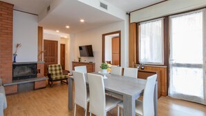 A dining area with a brick fireplace, a television, and a large window with curtains. - 2 bedroom gorgeous apartment in Omegna (Omegna)