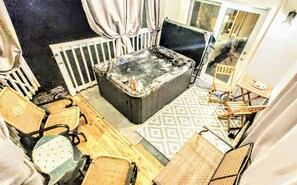 A room with a hot tub, wooden chairs, a patterned rug, and a view of the outside.