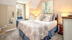 A bedroom with a large bed, two bedside lamps, a window, a mirror, and a painting on the wall. - 2BR/2.5BA, clean hot tub, spa tub, 1 mi to Pkway,10min to GSMNP, arcade,fire pit (Pigeon Forge)