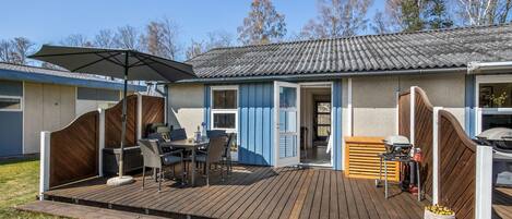 A patio area with a wooden deck, outdoor seating, and a grill.