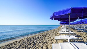 A beach with rows of white lounge chairs and blue umbrellas. - Nice apartment in Scanzano Jonico (Scanzano Jonico)