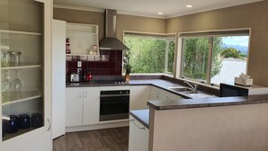 A modern kitchen with white cabinets, a built-in oven, a stainless steel sink, and a large window offering a view of greenery. - Large & Luxurious Family Home in a Private and Peaceful area  (Rotorua)