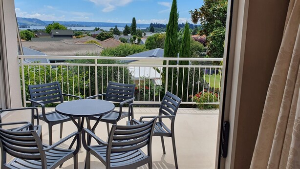 A balcony with a table and chairs, offering a view of houses and trees. - Large & Luxurious Family Home in a Private and Peaceful area  (Rotorua)