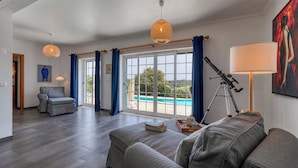 A spacious living room with a large window, a telescope, and a pool view. - Villa with private pool and large garden (Ribamar)