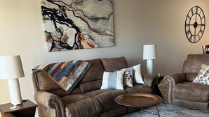 Ein Wohnzimmer mit einem braunen Ledersofa, einem gemusterten Sessel, einem Couchtisch und einem Teppich.