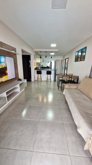 Ein modernes Wohnzimmer mit Fernseher, einer Couch und einem Essbereich mit Stühlen und einem Tisch.