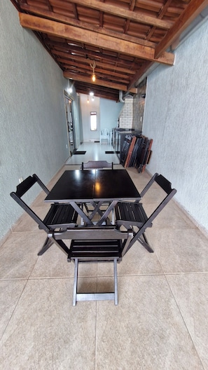 Un espace repas comprenant une table centrale et des chaises, un mur en briques et un plafond avec des poutres apparentes.