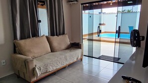 Een woonkamer met een bank, een televisie en een glazen schuifdeur naar een zwembad.