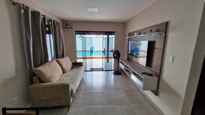 Ein Wohnzimmer mit Sofa, Fernseher und Blick auf einen Pool.