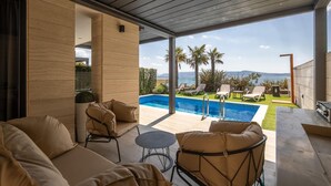 Un área de piscina moderna al aire libre con sillones de descanso y vistas al mar.