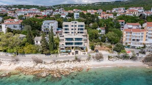 Zona residencial costera con edificios modernos, un litoral rocoso y aguas turquesas cristalinas.