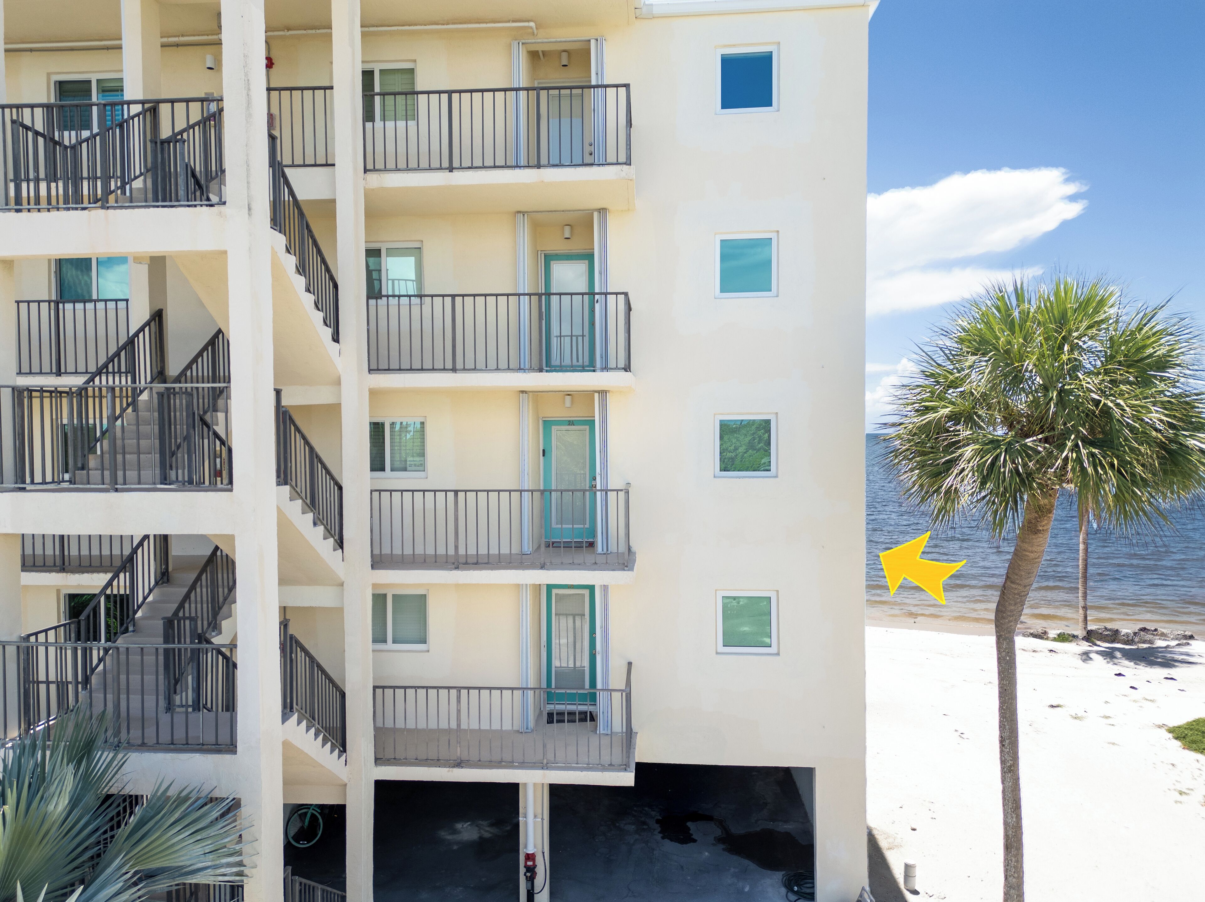 Un hotel de varios pisos con balcones, vista a la playa y una palmera.