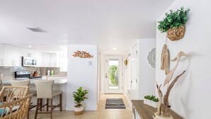 Une cuisine moderne avec des meubles blancs, un four à micro-ondes encastré et un coin repas doté de chaises en osier.