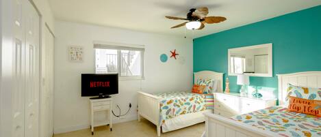 Un dormitorio con dos camas, ventilador de techo, televisor y ventana.