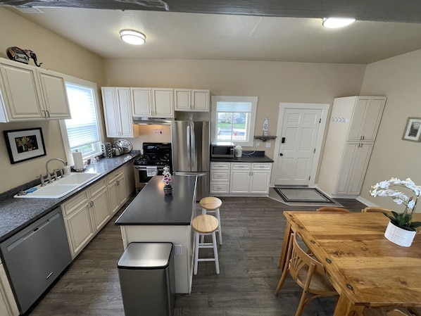A modern kitchen with white cabinets, stainless steel appliances, and a wooden dining table.