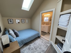 A bedroom with a skylight, a bed, a bedside table, a dresser, and a walk-in closet.
