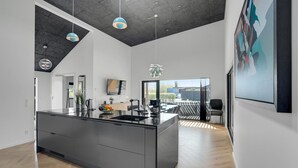 Uma cozinha moderna com uma ilha grande, área de jantar com vista e sala de estar com uma pintura.