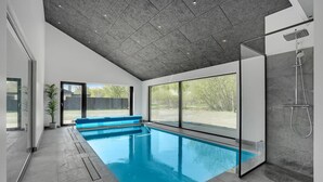 Uma piscina interior moderna com cobertura de vidro, um banco integrado e área de chuveiro separada.