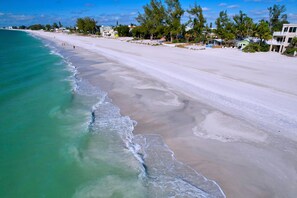 Una playa con agua turquesa cristalina, una amplia orilla de arena y varios edificios al fondo.