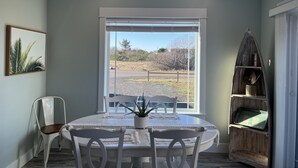 Un área de comedor con una mesa y sillas, un ventanal con vistas al exterior y una estantería de madera.